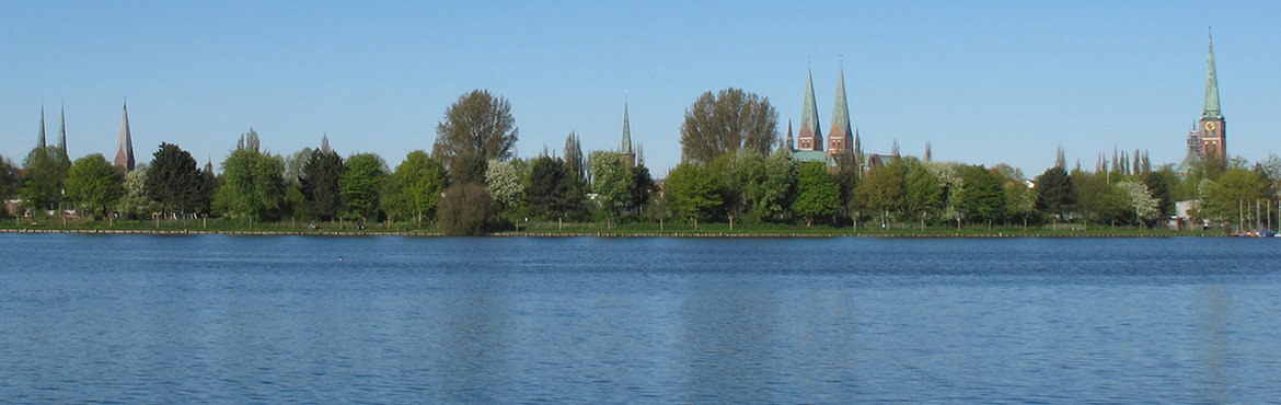 Die Wakenitz im Vordergrund, die Silhouette Lübecks dahinter, klarer blauer Himmel